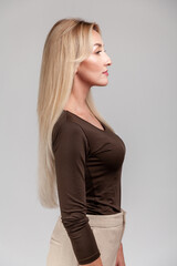 Fototapeta premium Calm middle aged woman standing in profile looking straight ahead wearing dark brown long sleeve shirt and neutral beige trousers standing isolated over gray background