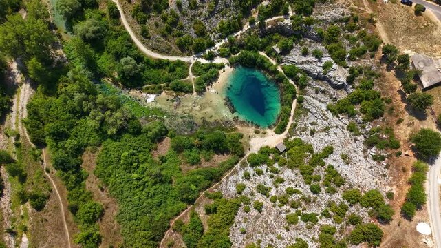 Aerial view of the Eye of the Earth, Cetina River Spring in Croatia, deep blue karst spring surrounded by green trees and rocky terrain