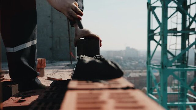Placing brick onto mortar on wall with tower crane structure in background