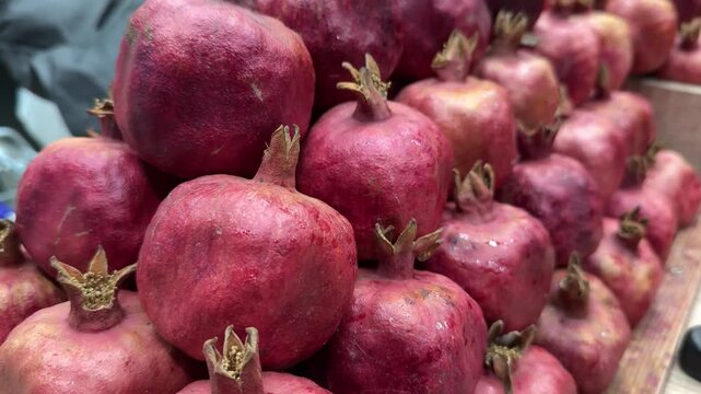 Close-up stacked pomegranates on rack, red mountain variety in wooden crate supermarket produce aisle, textured skin with light