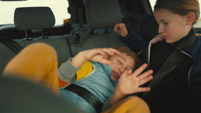 Playful little brother tickling sister in car