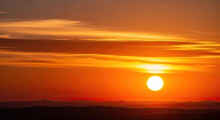 Fototapeta premium Golden sunset with a large sun, orange and yellow clouds, and a silhouette of a mountain range in the background. 