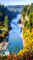 Obraz premium River flows through a gorge with autumn foliage, a bridge spans afar under a sunny sky