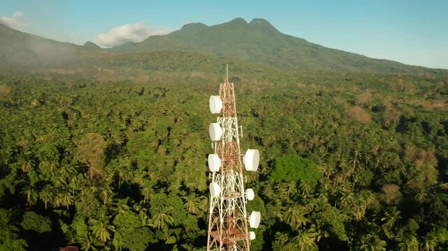 Telecommunication tower, communication antenna against mountains and rainforest, aerial view. Repeaters on a metal tower. Camiguin, Philippines