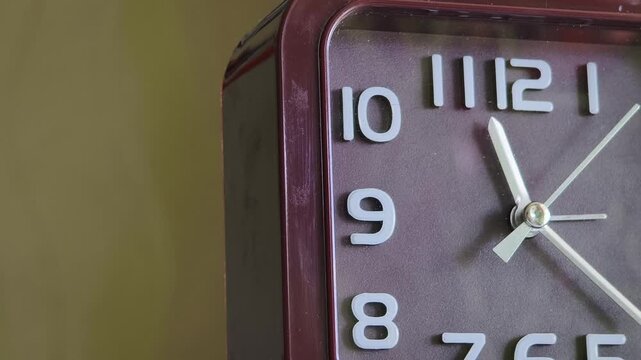 Macro view capturing the left side of a brown analog clock face with a ticking second hand. The rhythmic motion past large white numbers symbolizes precision and workflow.