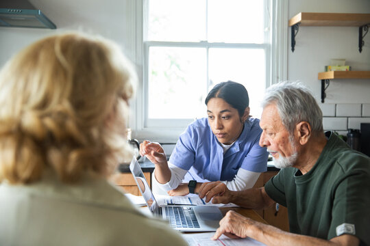 Caregiver assists senior couple with online paperwork at home