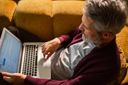 Middle-aged man working on laptop at home on sofa