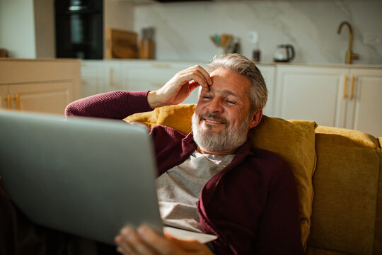 Smiling senior man using laptop on couch at home