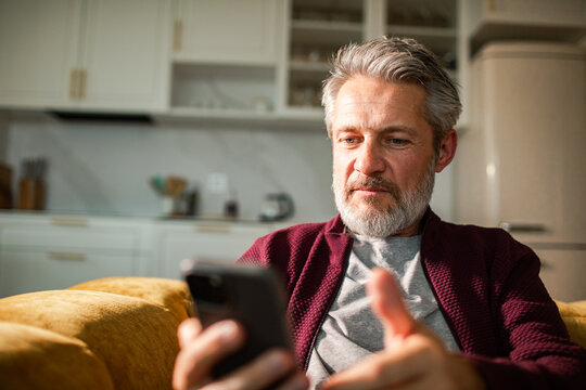 Middle-aged man using smartphone at home kitchen
