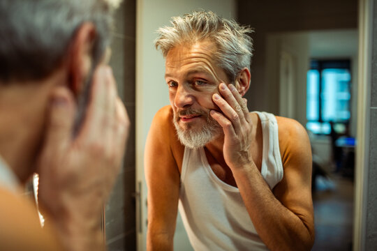 Mature man checking face in bathroom mirror at home