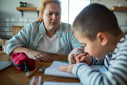 Concerned mother helping child with homework at kitchen table