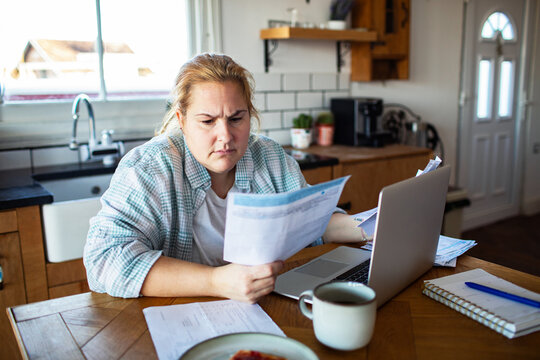 Concerned woman reviewing household bills on laptop at kitchen table