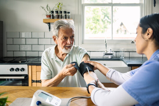 Nurse measuring senior man's blood pressure in home kitchen