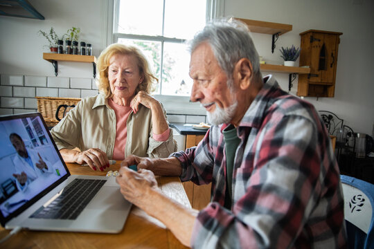 Senior couple consulting doctor via video call at home kitchen table