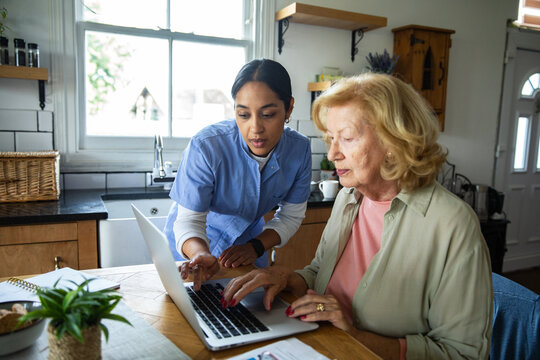 Home caregiver assisting senior with laptop in kitchen