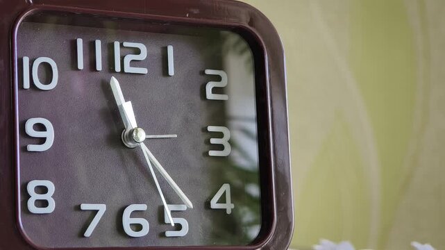 Extreme close-up of a square analog clock face with a brown dial and white numbers. The continuous motion of the second hand focuses attention on the passing of moments.