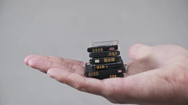 A mans open palm presents a stack of obsolete lithium-ion batteries. The shot symbolizes the growing issue of electronic waste and the need for proper disposal.
