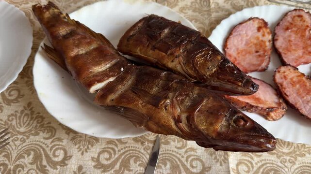 Smoked walleye and pork steaks plated on white plate with patterned tablecloth, golden crispy skin, sliced pork rounds