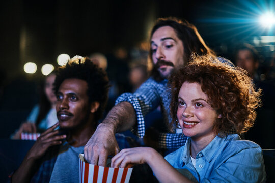 Friends sharing popcorn while watching a movie in a cinema