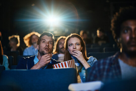 Couple eating popcorn while watching movie at the cinema
