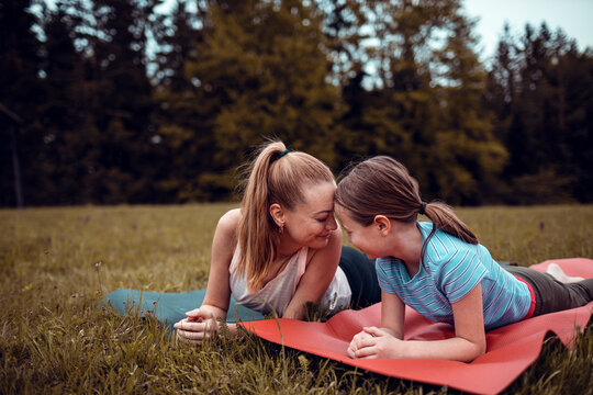 Mother and daughter bonding on yoga mats outdoors in a grassy park