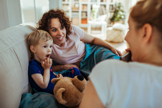 Two women with toddler relaxing on sofa at home