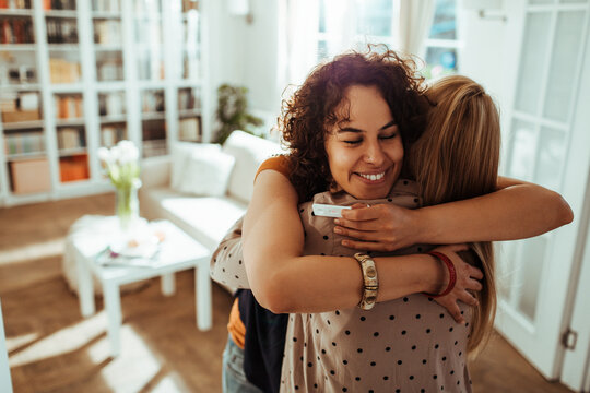 Two women hugging with positive pregnancy test at home