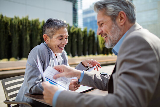 Smiling senior professionals reviewing documents at outdoor cafe