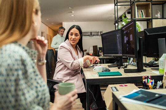 Coworkers collaborating at dual monitors in modern office