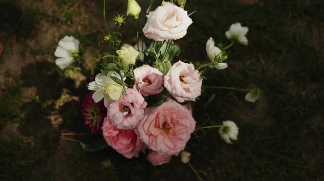 A soft pink bouquet on the grass: a cinematic close-up taken during the golden hour, featuring lisianthus and roses arranged for a wedding