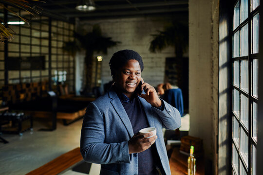 Smiling businessman talking on smartphone by cafe window with coffee