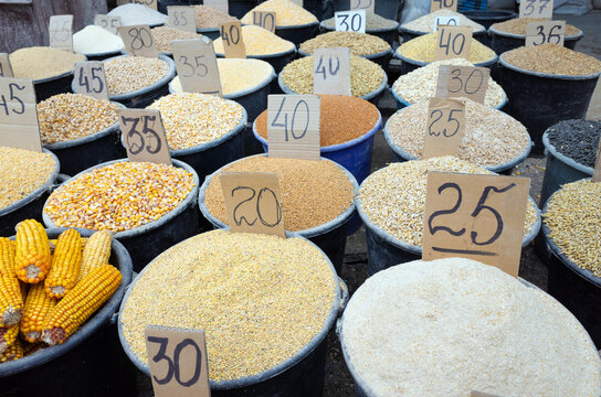 Assorted organic grain types and cereals in buckets stand at outdoor street market. Hand-written price tags on cardboard placed in each container with various grain and cereals supplies 