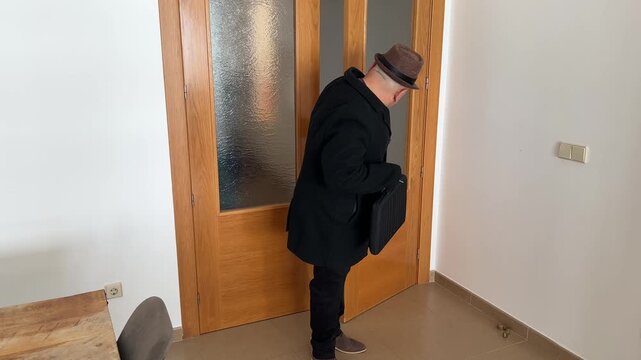 Hombre llegando a casa, dejando sus cosas y quit&aacute;ndose el abrigo