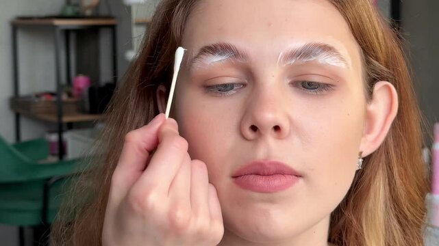 A young girl during a professional procedure of mapping and correction of eyebrows with lamination. The master does permanent eyebrow styling using hair coloring.