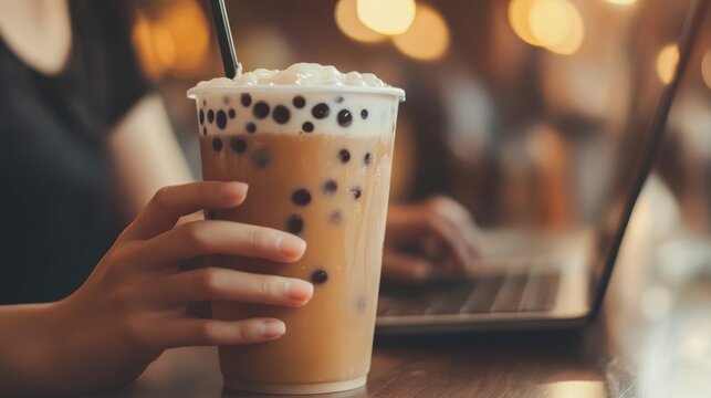 A person holding a cup of bubble milk tea with cream