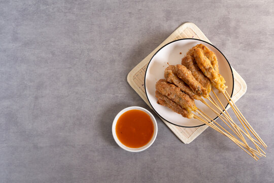 Sempol ayam skewers served on a plate with spicy chili sauce on dark background. Sempol made from chicken, spices and eggs. Popular Indonesian street food snack. Top View