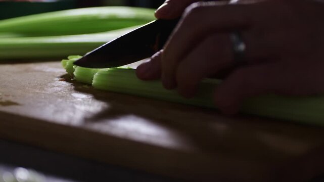Detail of woman hand cutting celery stalks on cutting board. Home preparing food for cooking, lifestyle