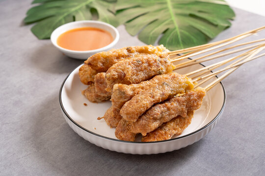 Sempol ayam skewers served on a plate with spicy chili sauce on dark background. Sempol made from chicken, spices and eggs. Popular Indonesian street food snack. Close up