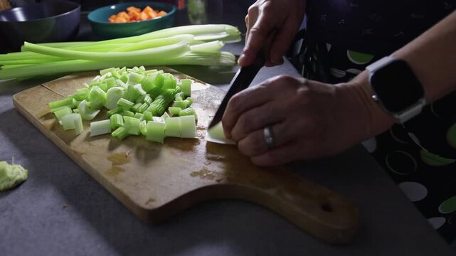 Detail of woman hand cutting celery stalks on cutting board. Home preparing food for cooking, lifestyle