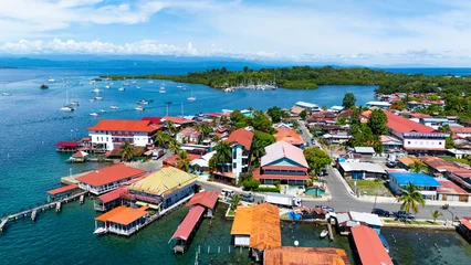 A stunning aerial drone view of Isla Colón showcasing crystal-clear turquoise waters, lush tropical vegetation, and colorful Caribbean-style buildings along the coastline. © cris