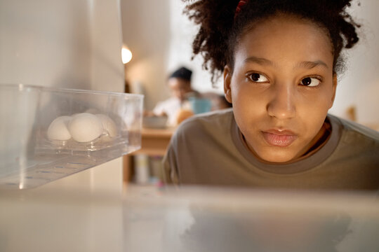 Close up of Black teenage girl looking into nearly empty refrigerator, checking limited food at home and expressing household poverty. Useful for food insecurity, low income family, hunger campaigns