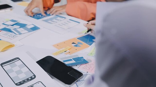 Asian women working together as web designers in an office, pointing at whiteboard with uxui mobile app wireframe