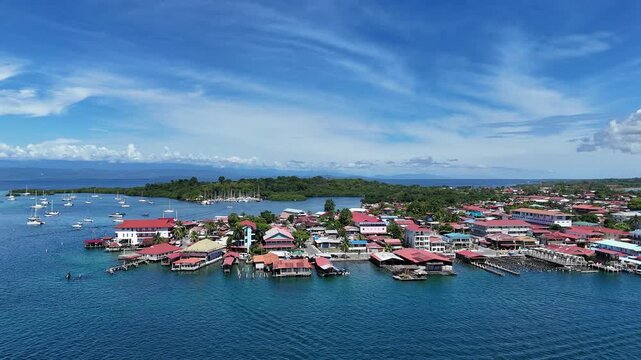 A stunning aerial drone view of Isla Col&oacute;n in Bocas del toro Panama,showcasing crystal-clear turquoise waters, lush tropical vegetation, and colorful Caribbean-style buildings along the coastline. 