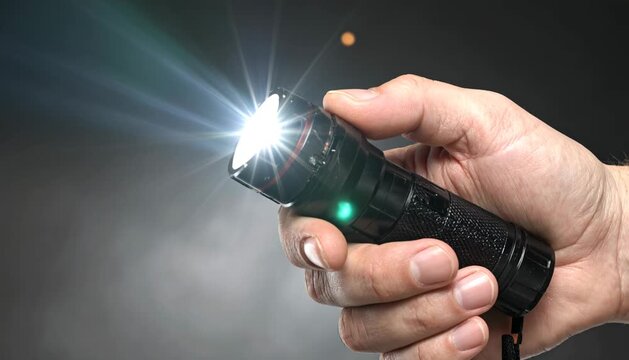 Close Up of a Hand Holding a Bright Tactical LED Flashlight in the Dark
