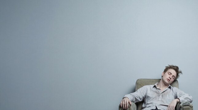 Exhausted young man sleeping in an armchair against a grey wall background