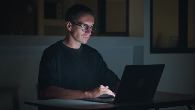 Man working on laptop at night from home, focused on screen and typing quietly. Remote work lifestyle shows digital job, online tasks, work from home and flexible modern career