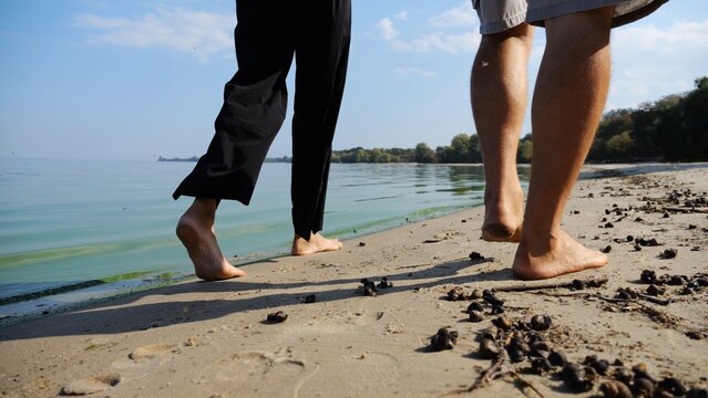 Bare feet of couple stepping together along sand beach at coastline. Male and female legs of pair walking near seaside. Happy lovers going along sandy shore. Concept of summer vacation or holiday