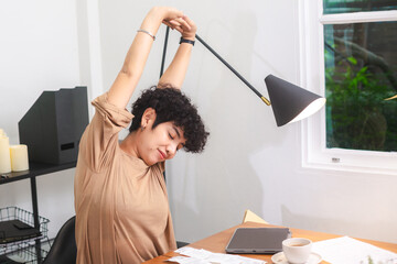 Obraz premium Young woman stretch curly hair casual shirt home office modern lamp natural light wooden desk window view relaxed pose morning routine asian woman freelancer remote work paperwork tablet cup