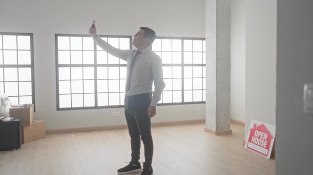 Man in shirt and tie holding smartphone and taking photos of empty room during open house inside building; focused.