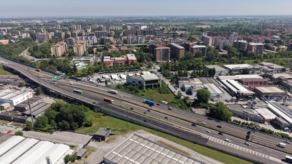Obraz premium Urban Aerial View: An expansive cityscape unfolds under a clear sky, with a modern highway cutting through the heart of the metropolis, showcasing urban growth and infrastructure.